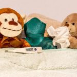 Two sick teddy bears with tissues, hot bottle, and thermometer.
